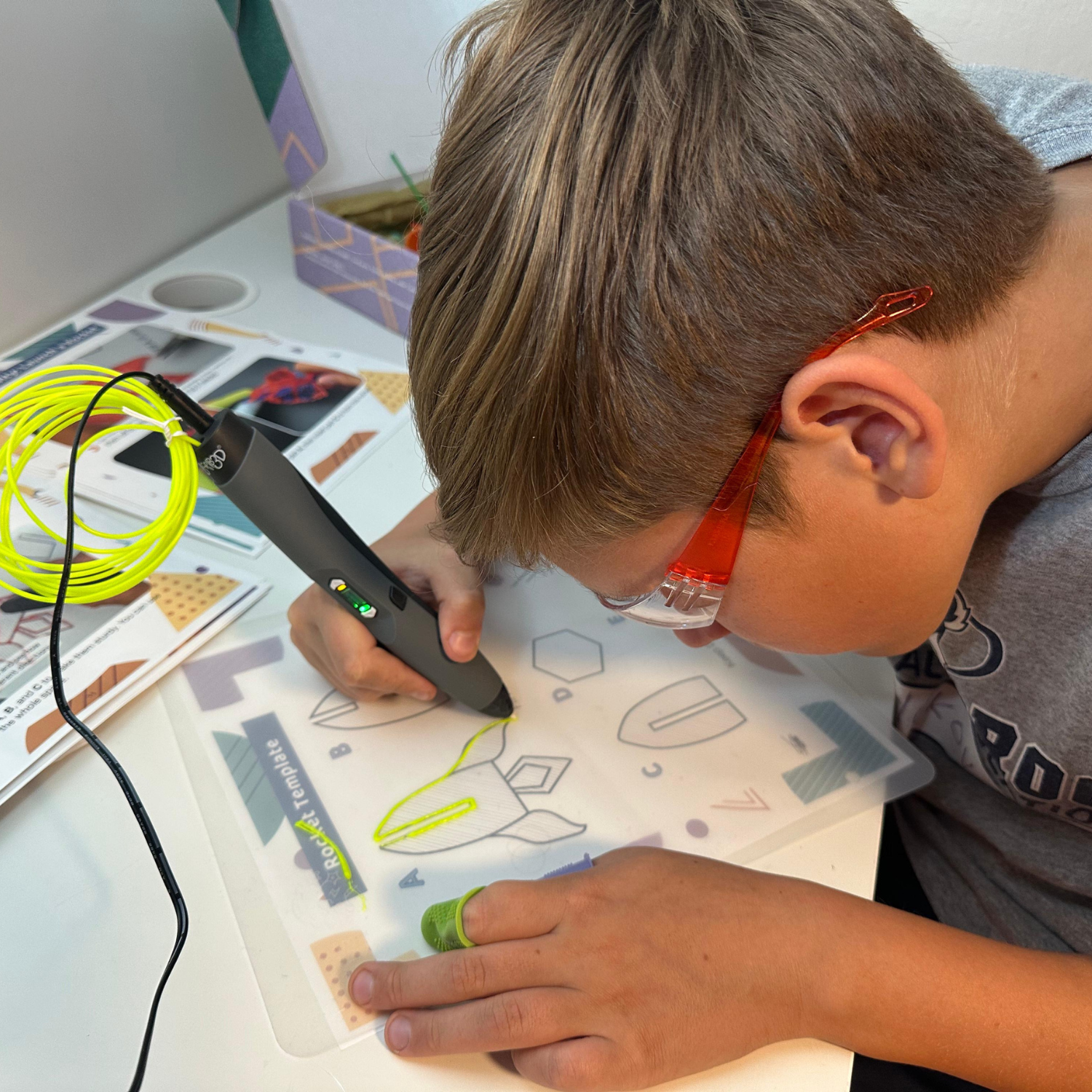 Child using a 3D pen STEAM kit with safety goggles, following the Enki photo curriculum
