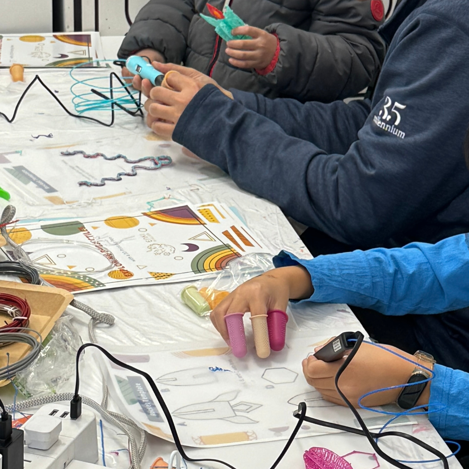 Hands-on 3D pen building — child tracing the Enki curriculum template with finger caps